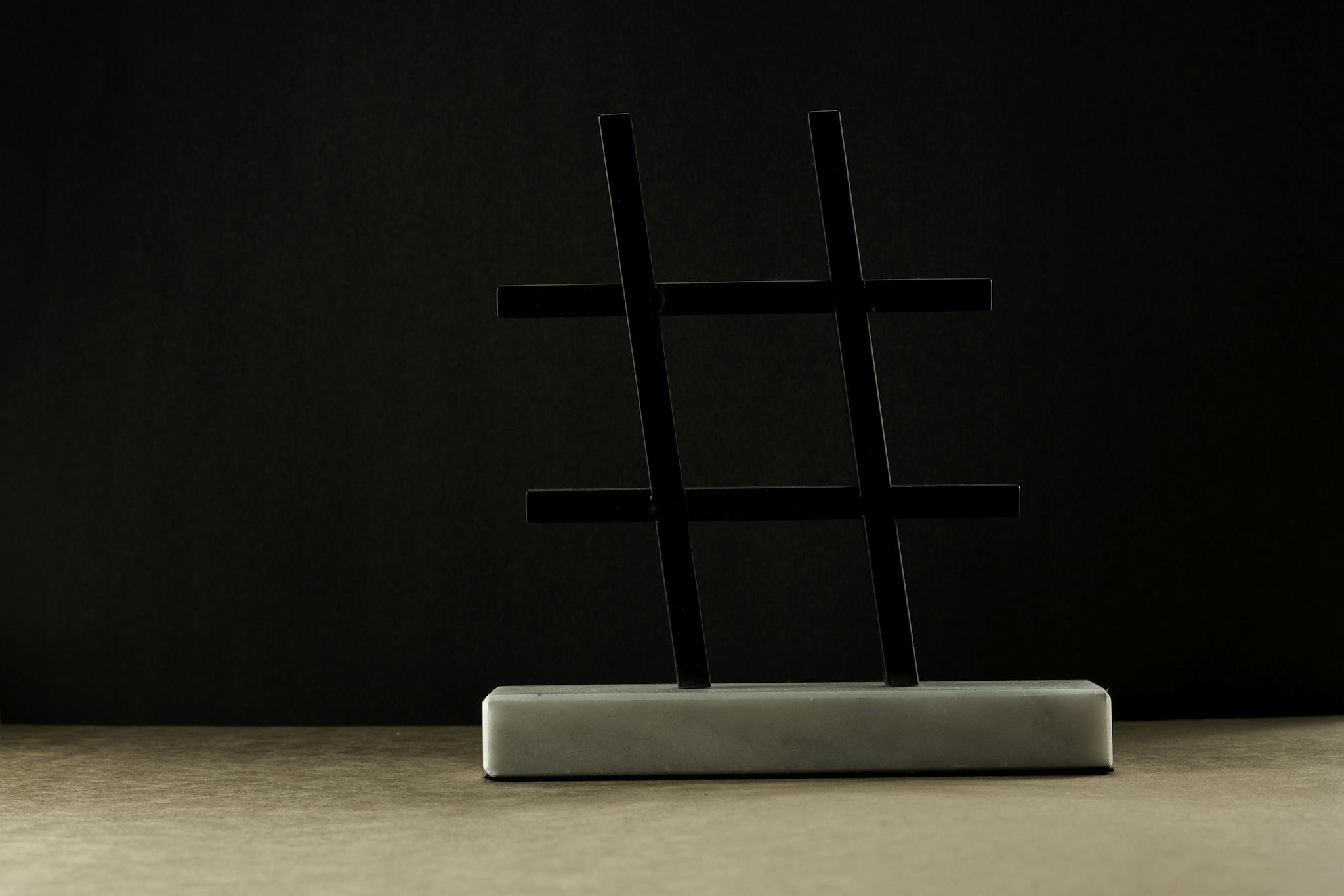 A modern hashtag sculpture in a minimalist setting with a dark backdrop.