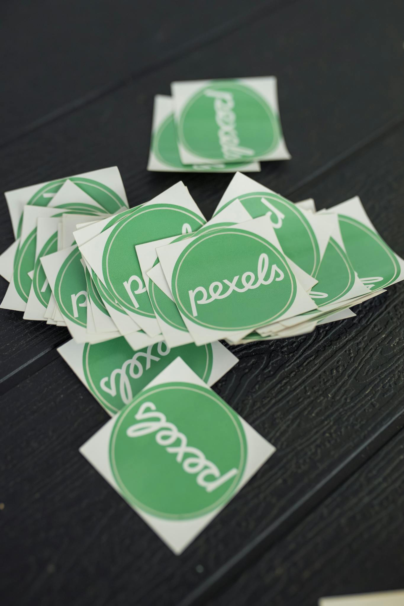 A scattered pile of green Pexels logo stickers on a textured dark surface, perfect for branding visuals.