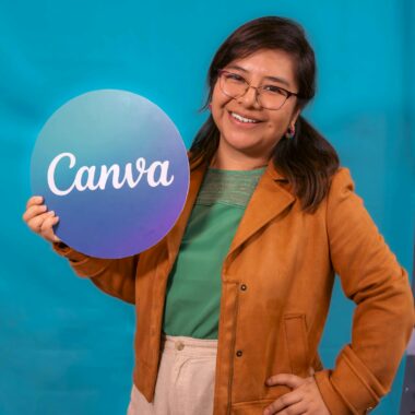 A smiling woman in a casual outfit holds a Canva sign, posing confidently against a vibrant blue backdrop.