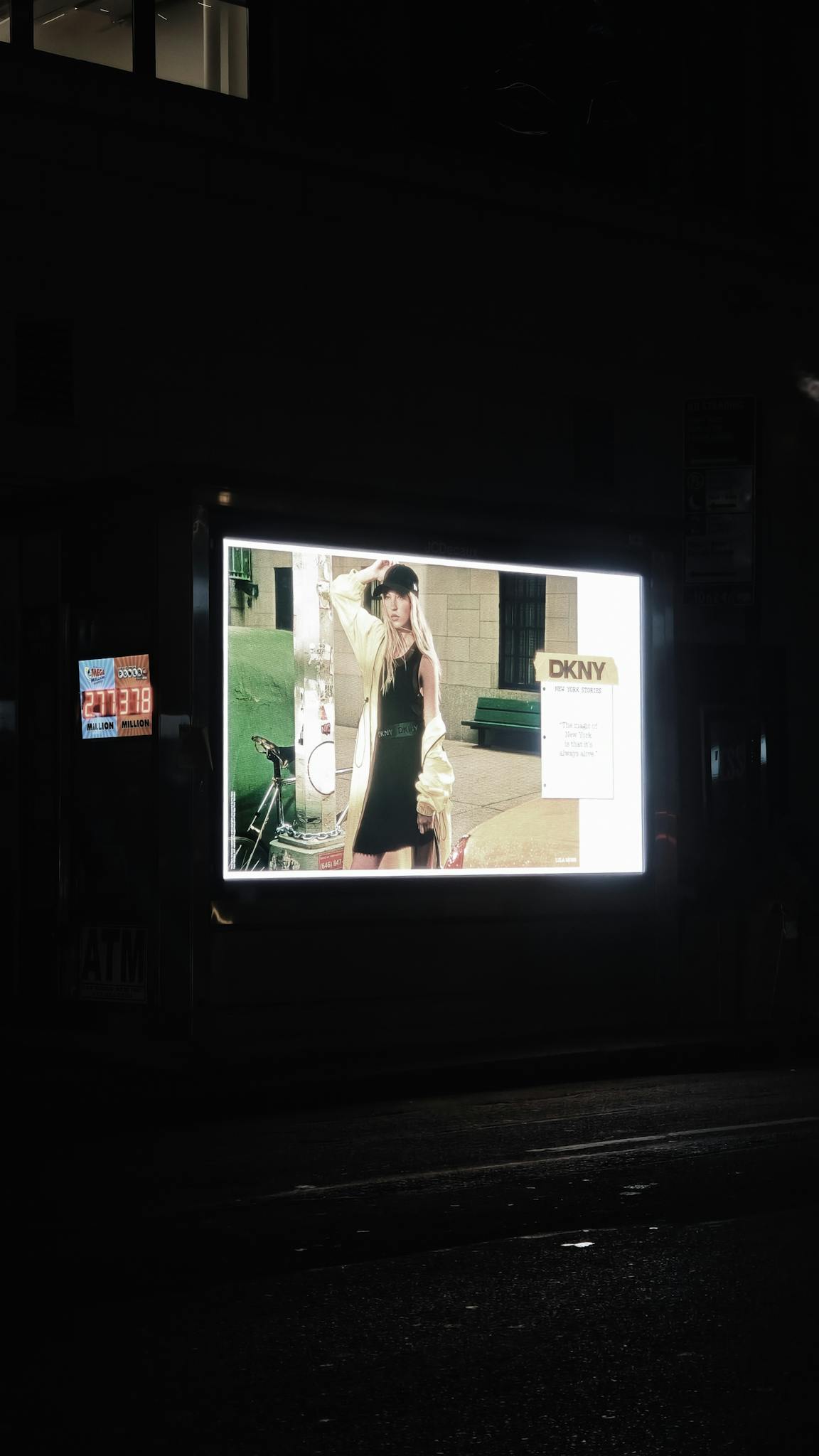 Outdoor illuminated fashion billboard featuring DKNY advertisement at night on a city street.